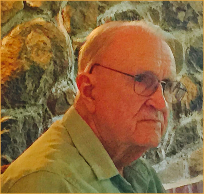 an older man wearing glasses sits against a wall