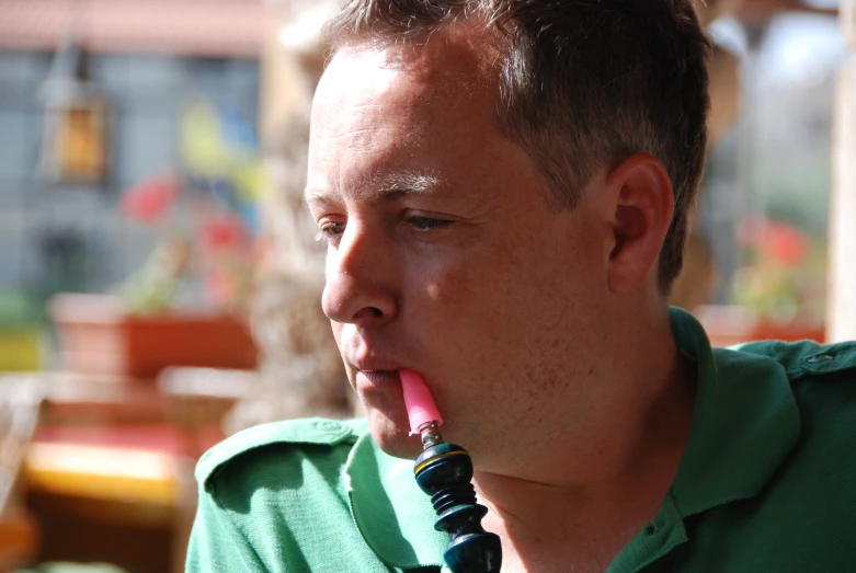 a man in a green shirt holding a plastic pink pen in his mouth