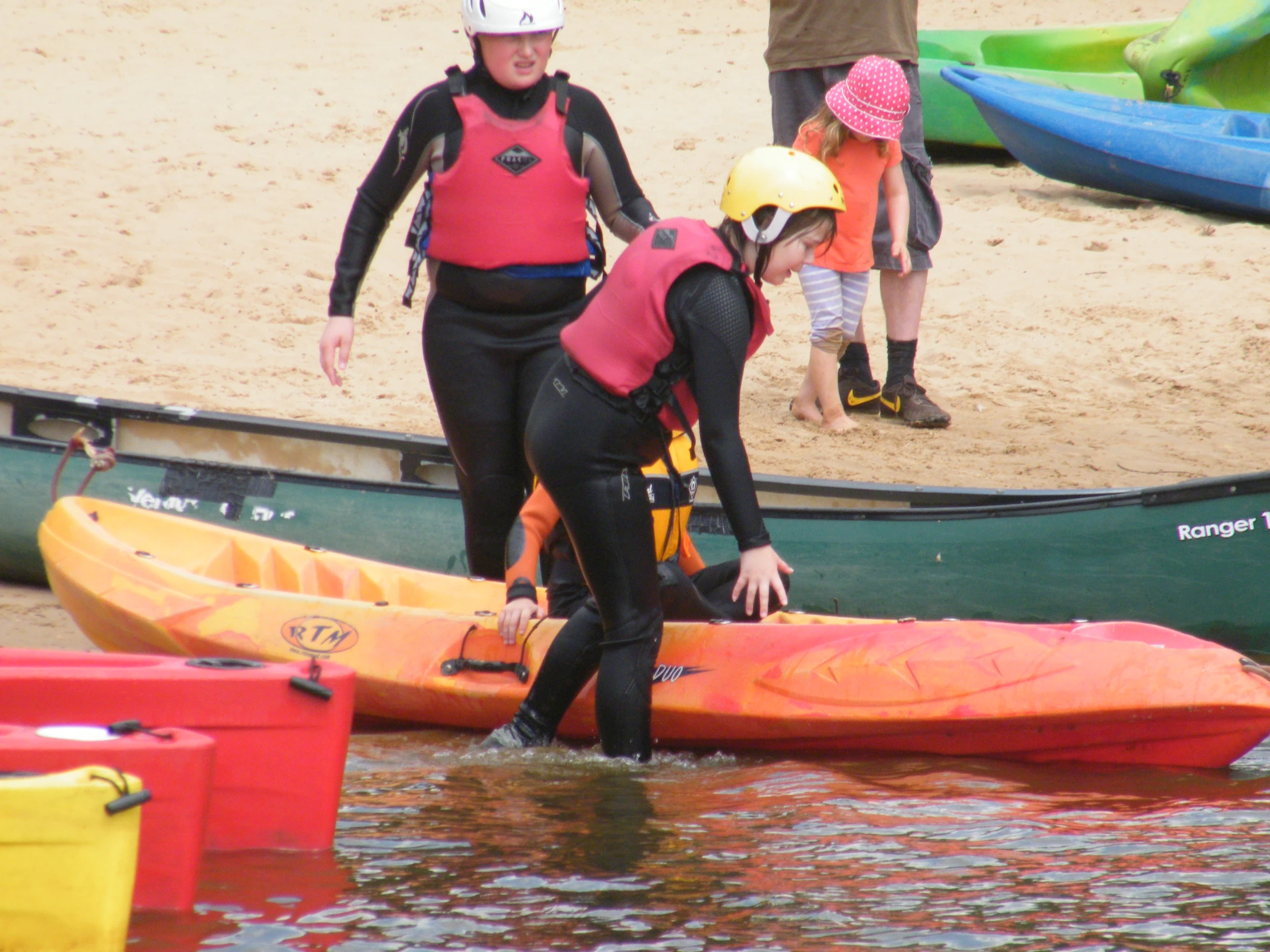 a woman is setting up kayaks near a group of children