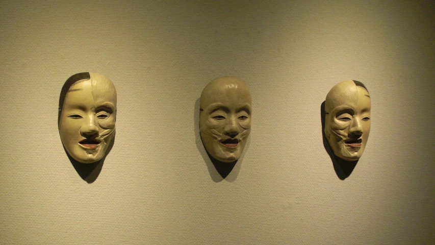 three masks with facial features on display in an art gallery