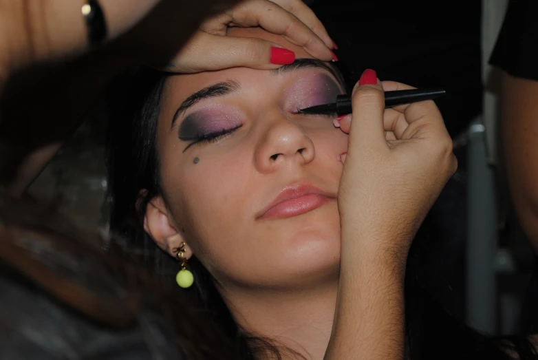 a woman putting lipstick on her face and putting her hands in her ears