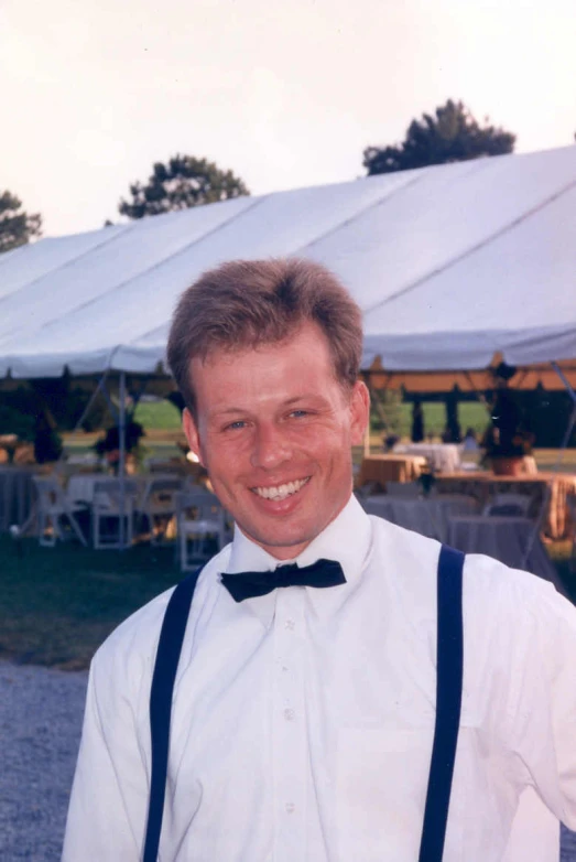 man in bowtie standing next to tent with table on grass