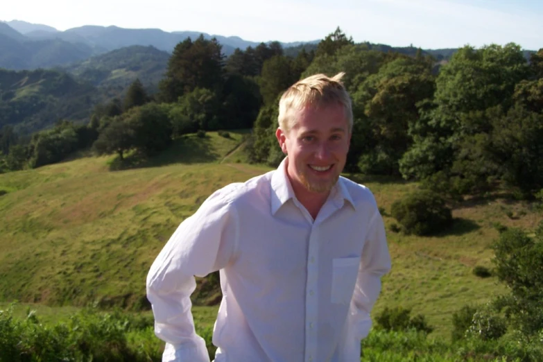 a man smiles in a scenic area of trees and mountains