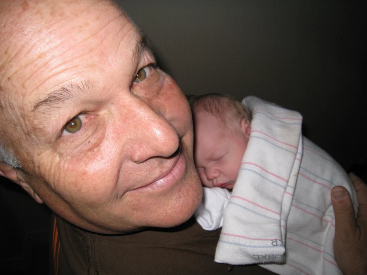 an older man holding his sleeping baby wrapped in a blanket