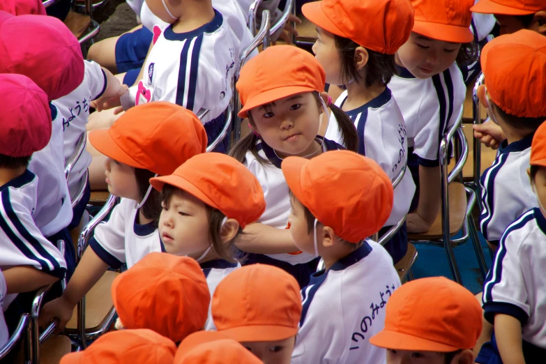 several children standing in rows, all wearing orange hats