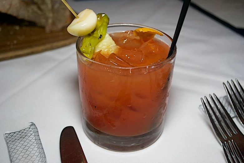 a drink with an orange and pickle garnish sits on a table