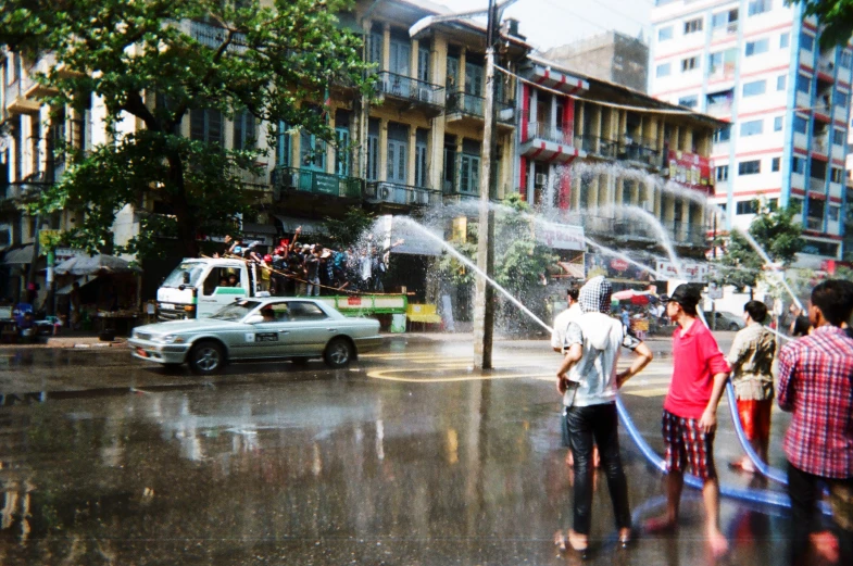 a street scene with people standing in front of a car spraying water