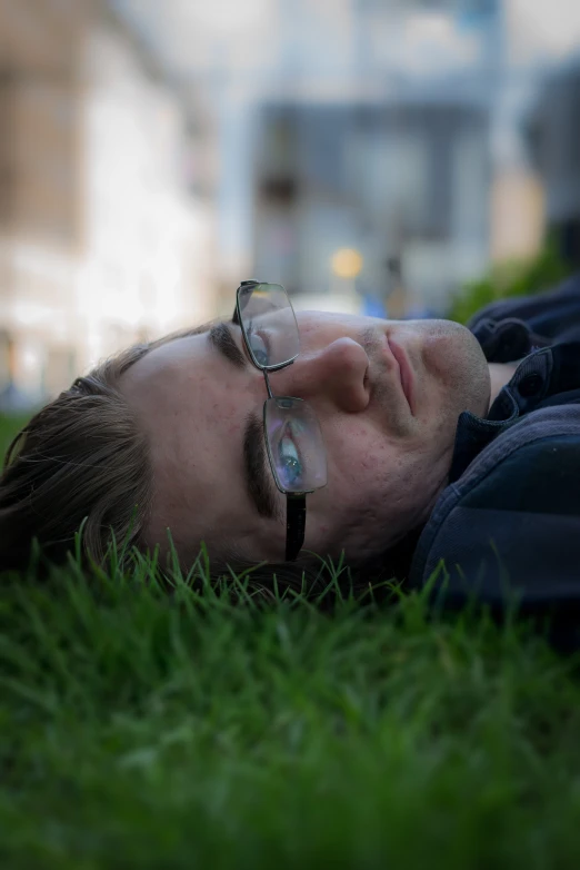 a man lying on the grass in the sun wearing glasses