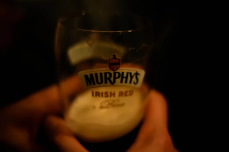 a hand holding a glass of beer with soing white inside