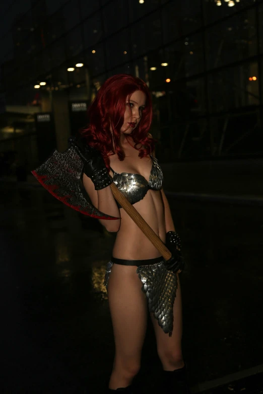 a woman with red hair, wearing silver lingerie, and carrying a wooden stick
