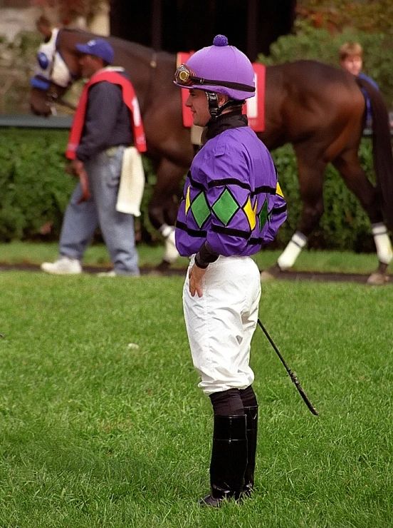 a jockey stands next to his horse, which runs behind him