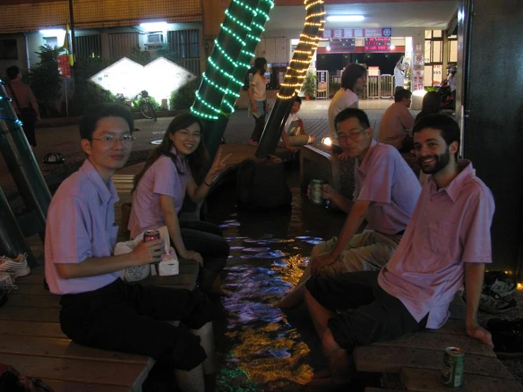 four young men and one woman sitting in front of a river with lights