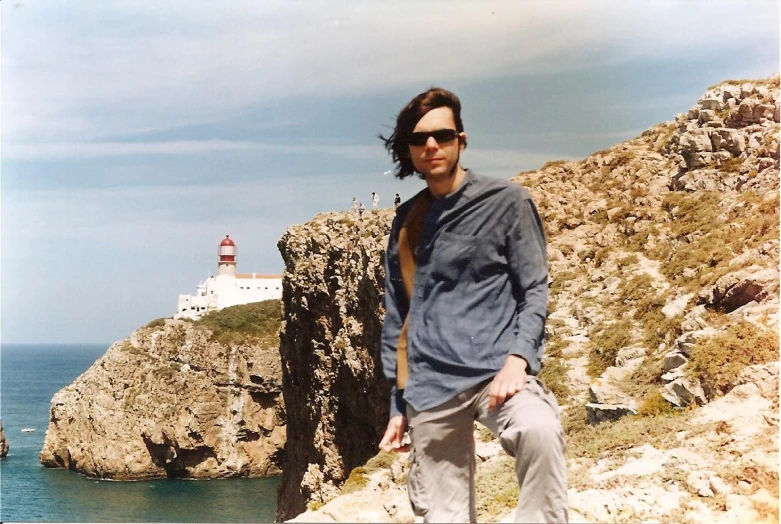 a man posing in front of a lighthouse in the distance