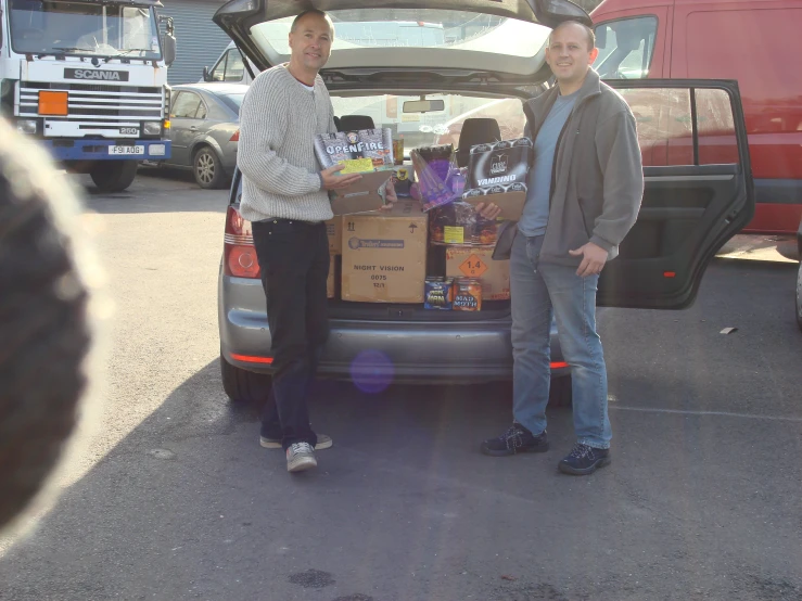 two people standing next to the trunk of a minivan