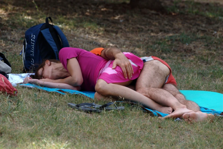 a couple is sleeping on a blue blanket in a park