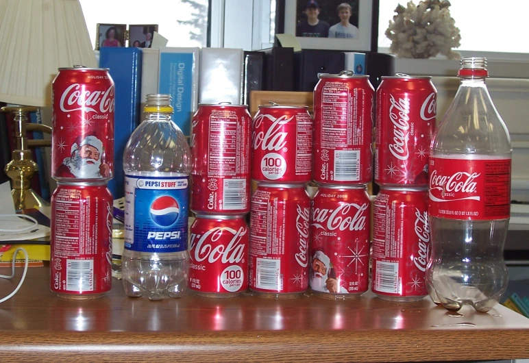 several soda cans and one glass on a desk with another bottle sitting next to it