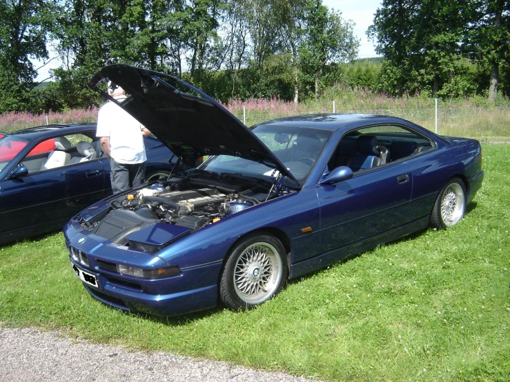 a blue sports car sits on grass next to two other cars