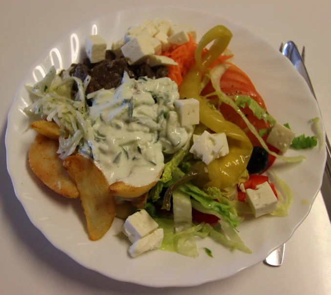 a plate of food containing fried potatoes, salad, cheese, and dressing