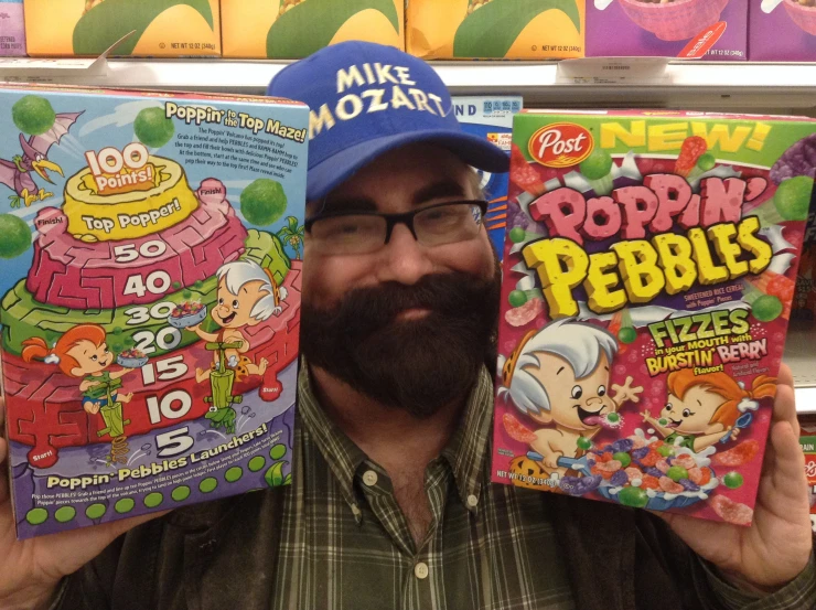 a man holds two books and stands in front of colorful shelves of cereal