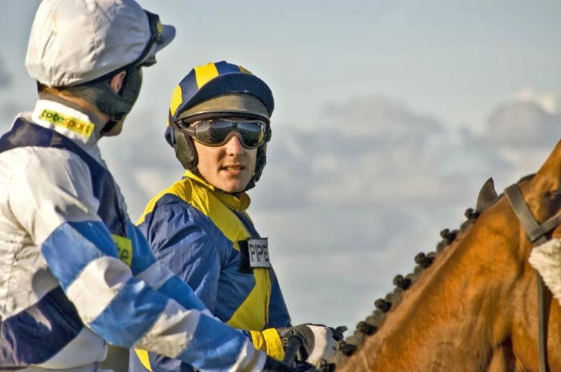 two jockeys in yellow and blue outfits on horses