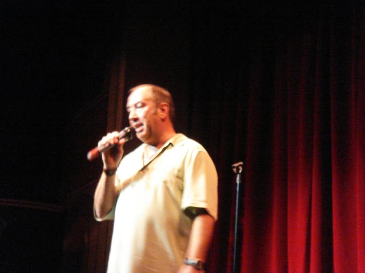 a man standing in front of red curtains while singing into microphone
