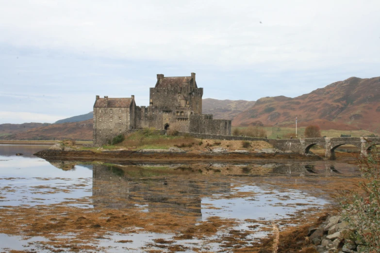 a castle surrounded by brown land with a stone bridge in the foreground