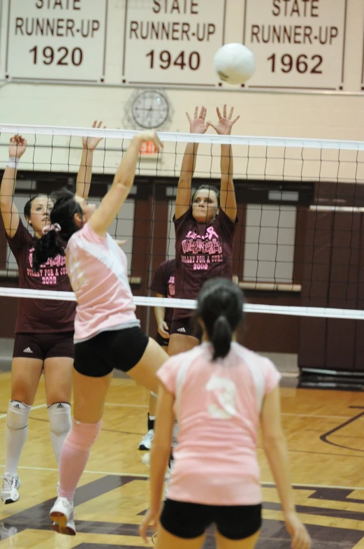 two girls playing volleyball in a gym with a ball