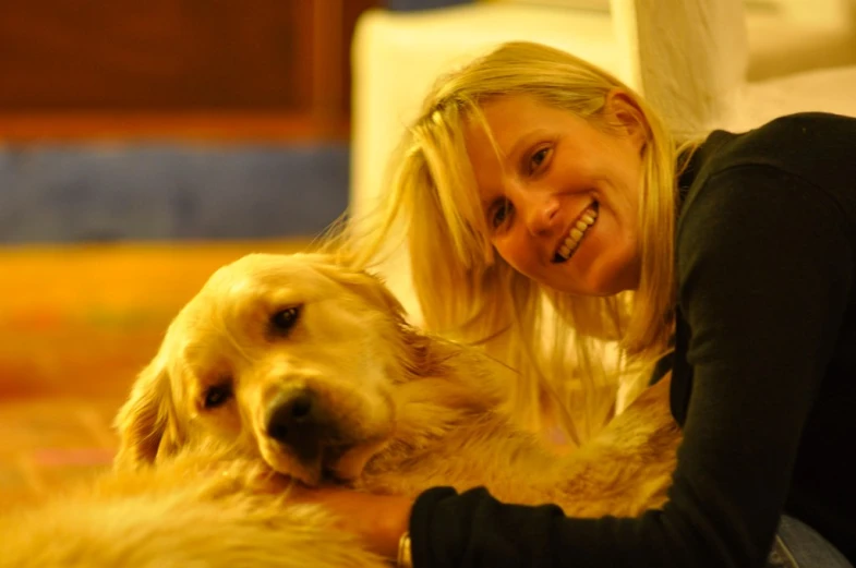 a smiling blonde woman sitting on the ground with a large golden retriever dog