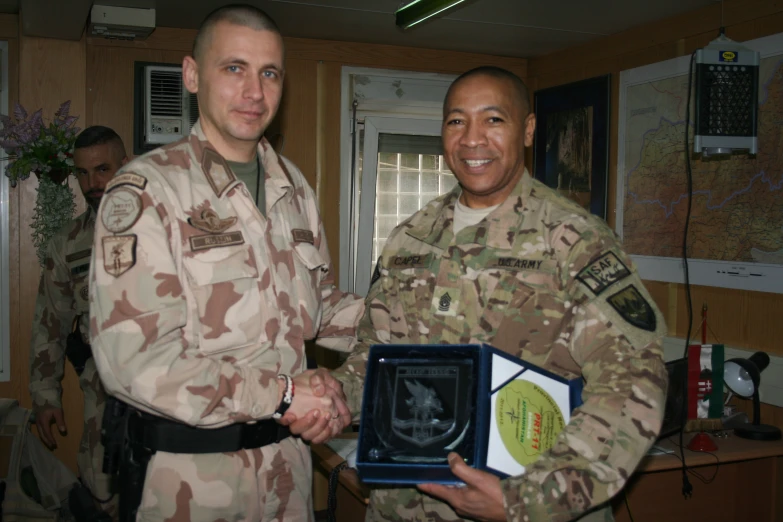 two soldiers hold up a plaque and smile at the camera