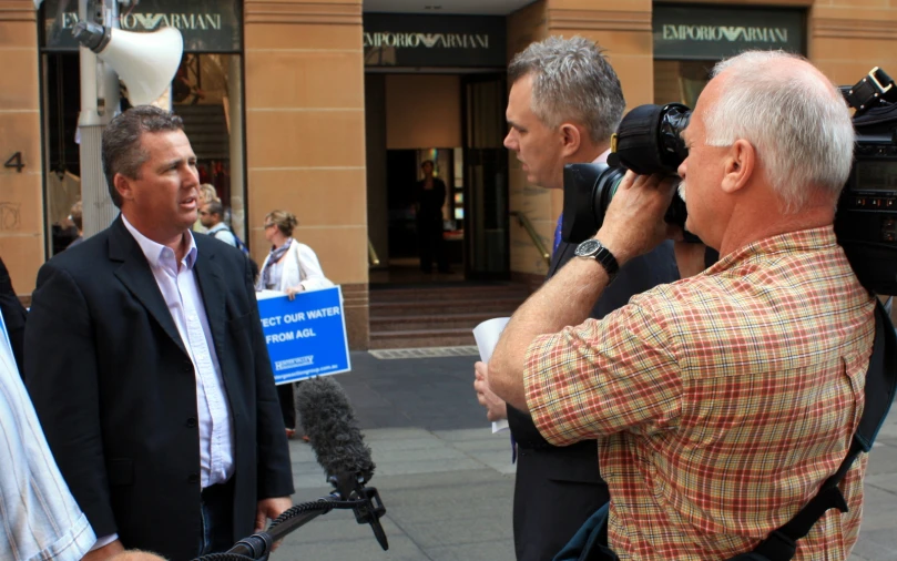 two men on the street one holding a camera and one with a news crew