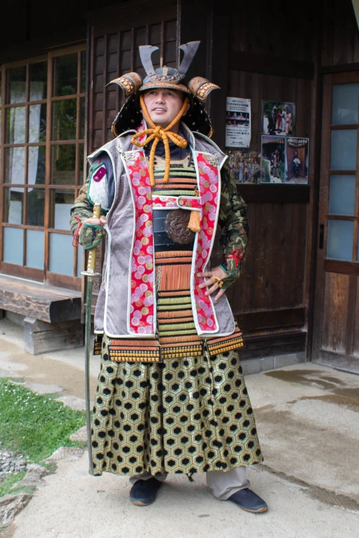 a man wearing elaborate clothing and large, metal horns stands in front of a wooden building