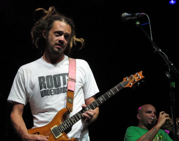 a man with dreadlocks plays his guitar on stage