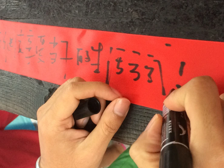 two people holding pens over a sign with asian characters on it