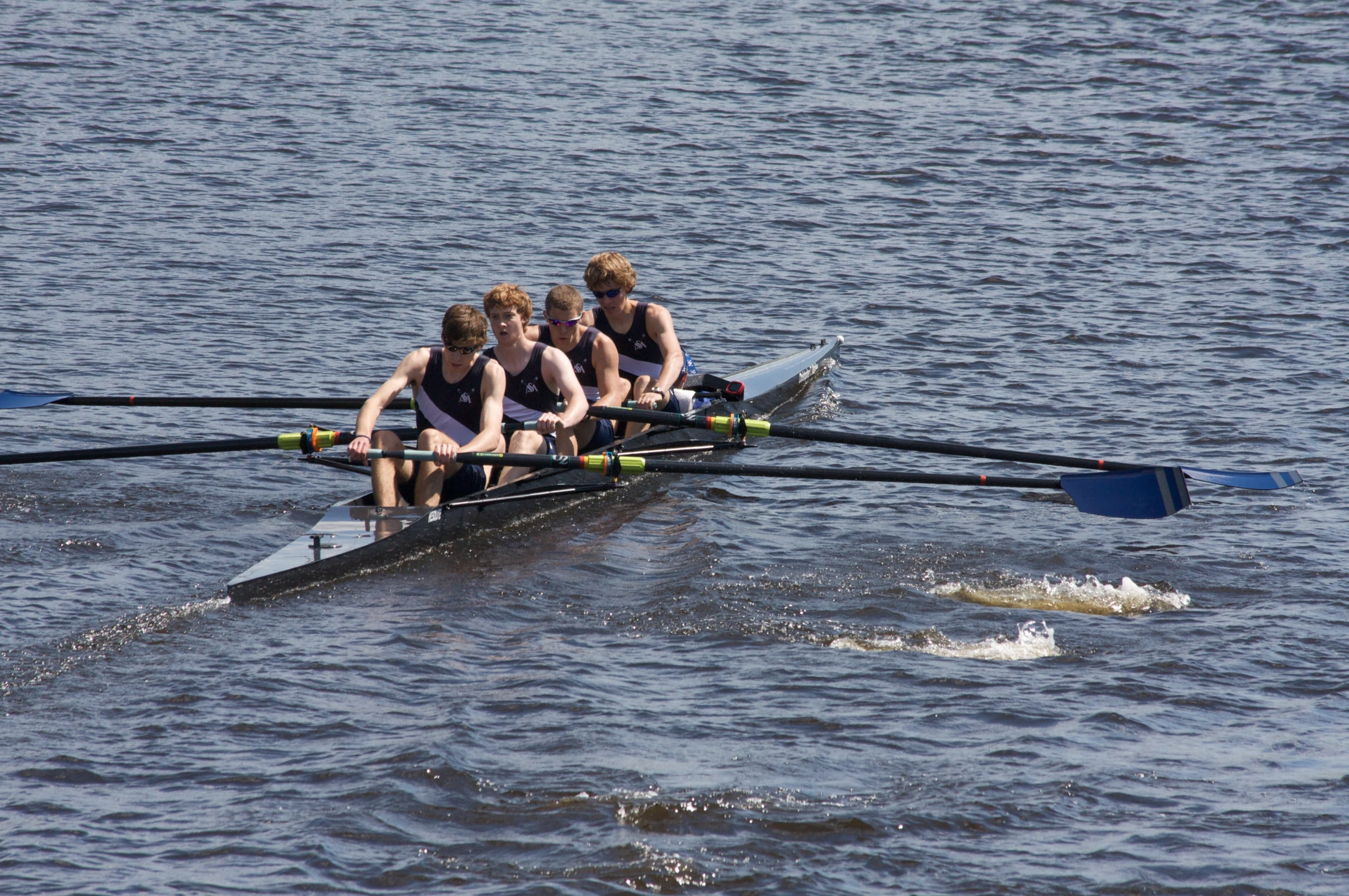 four people rowing in a single boat on the water