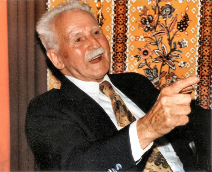 an older man wearing a suite is holding a cell phone