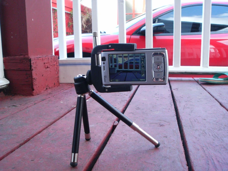 a red car behind a tripod, with a video camera in the foreground