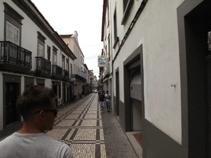 two people walking down an alley way in front of buildings