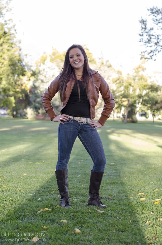 a young woman in jeans, boots and leather jacket poses for a picture