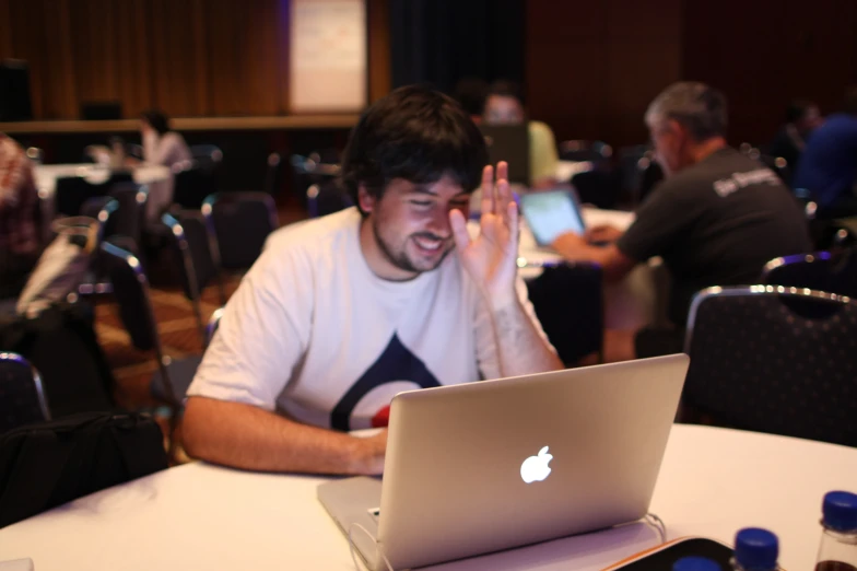 a man sitting at a table with a laptop and clapping