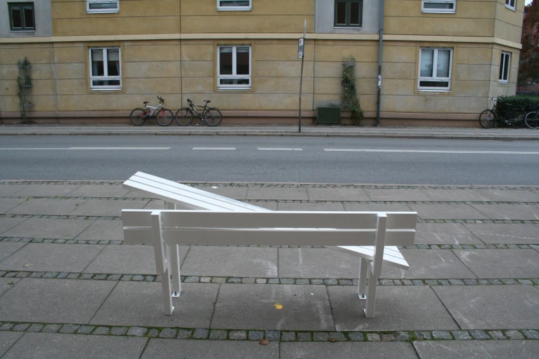 an empty white bench sitting on the sidewalk