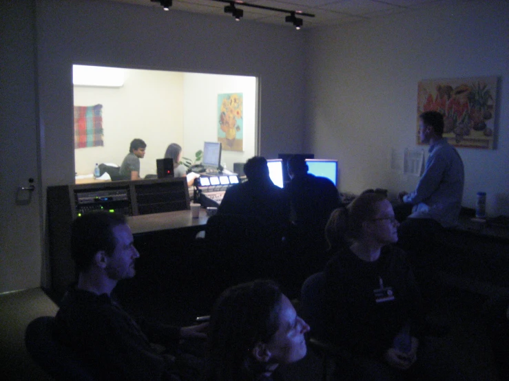 people standing in a dark room watching a man sitting in front of his tv