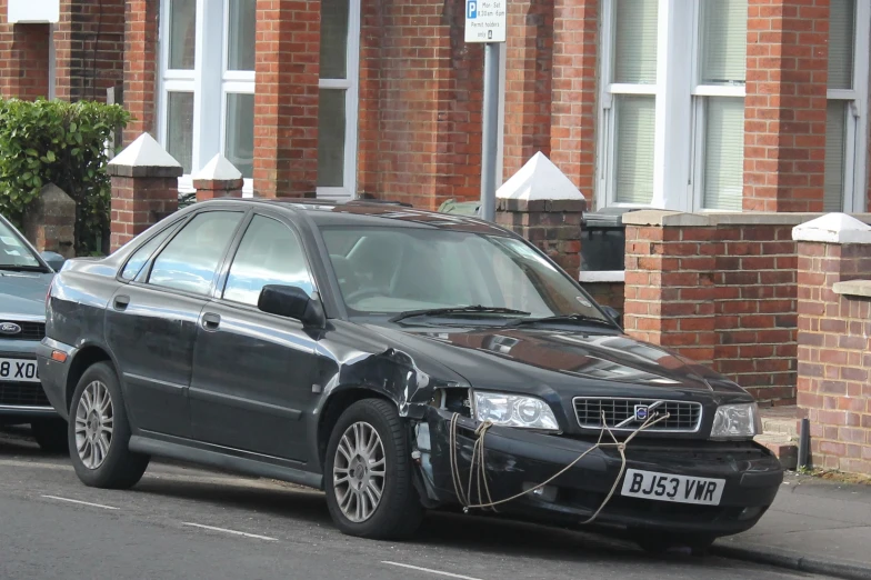 a black car in front of a red brick building with a tow hook attached to it