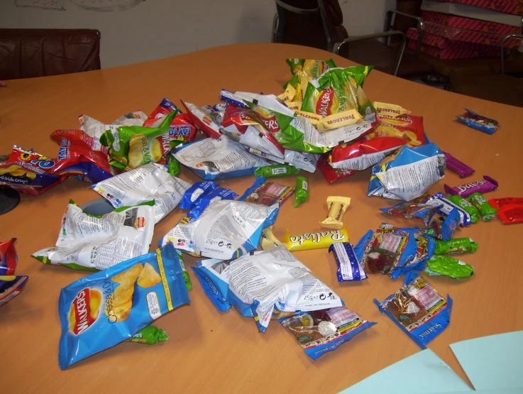 an assortment of chips and candy bags are all scattered on a wooden table