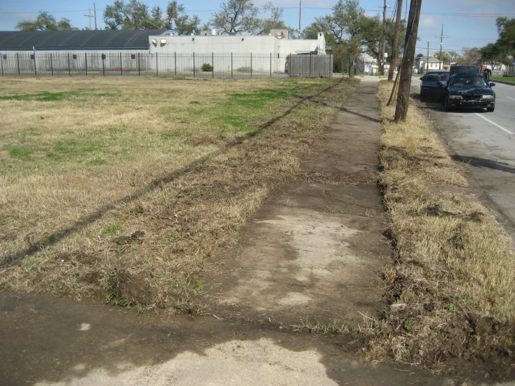 a sidewalk next to an empty yard with grass growing around