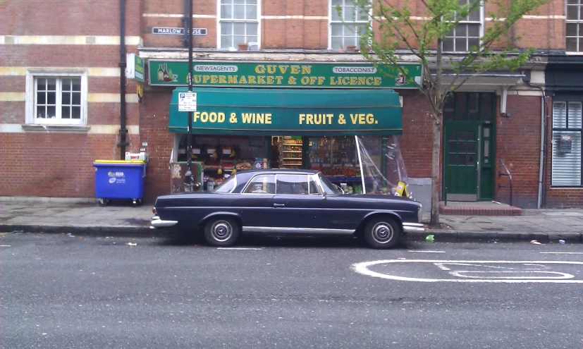 an old car parked outside of a green store front