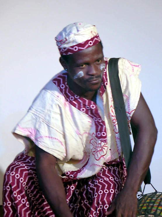 a black man wearing a red and white cloth sitting next to a suitcase