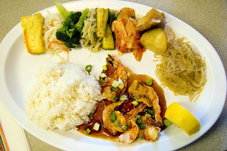 a plate of food with shrimp, rice, lemon wedges and sauce