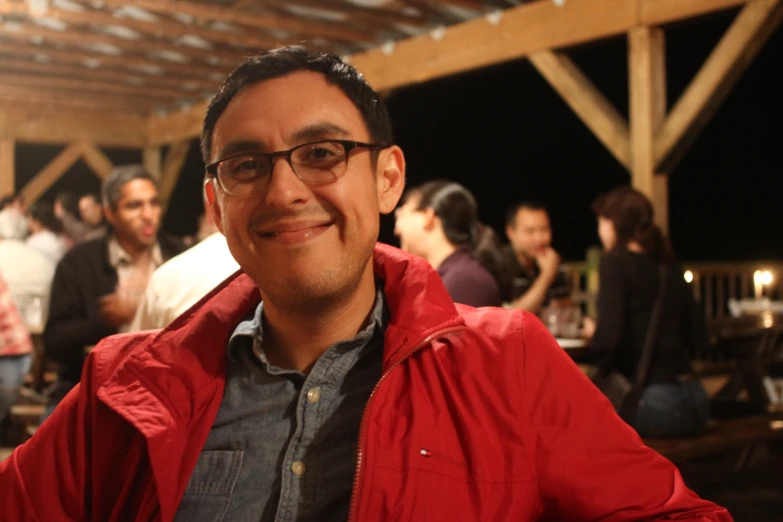 smiling man in red jacket and glasses at outdoor venue