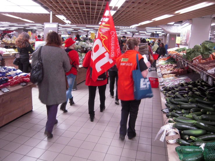 several people shop together in a market with signs and vegetables