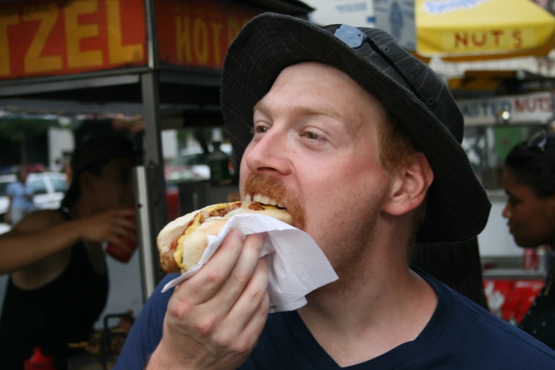 a man wearing a fedora takes a bite out of a  dog